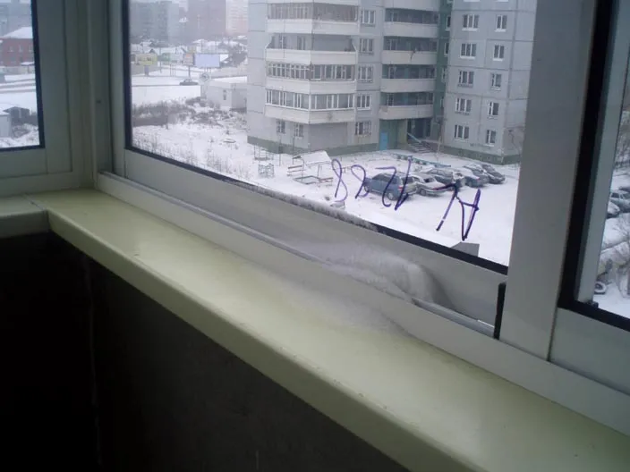 Снег на направляющей раздвижного окна на балконе